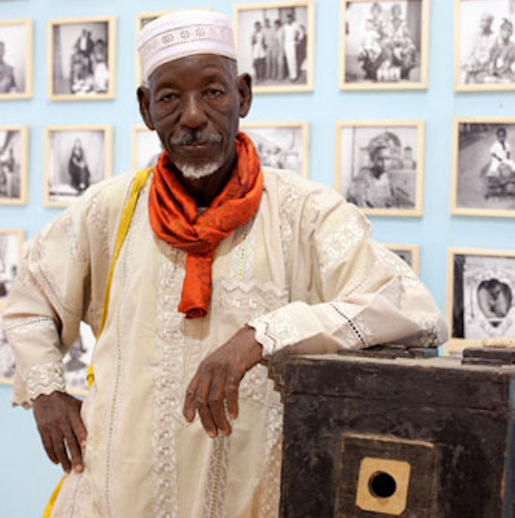 Photo: Oumar Ly poses with his first camera at Fes­ti­val mon­dial des Arts Nègres held in Dakar, Senegal from 10-31 December 2010. Credit: Wikimedia Commons.
